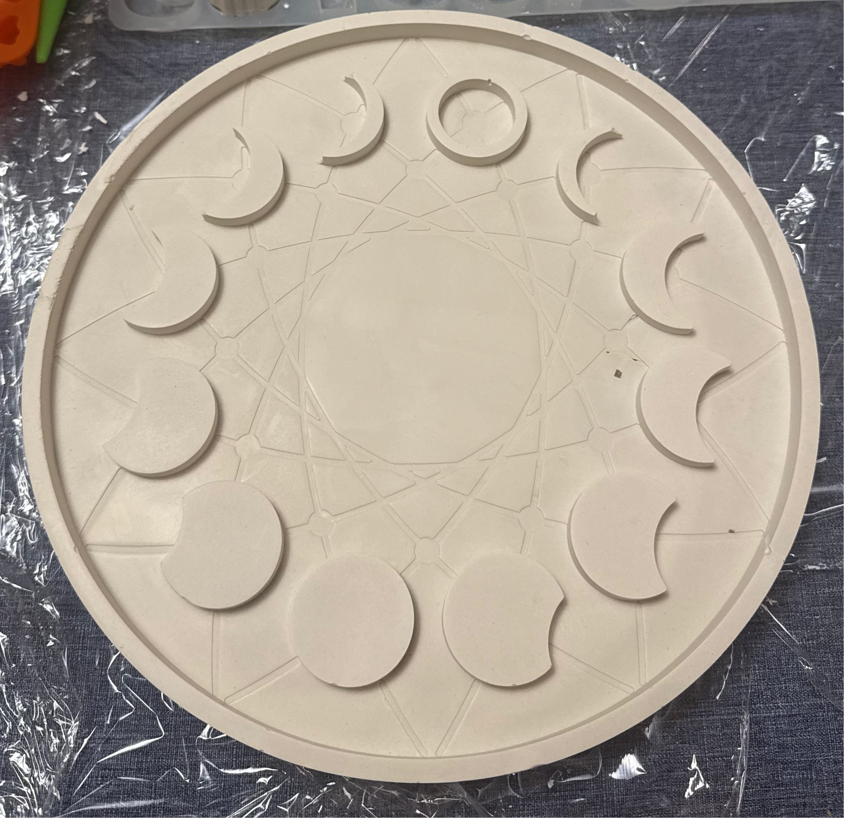 A round off-white silicone mold or tray with moon phases and a central star design.